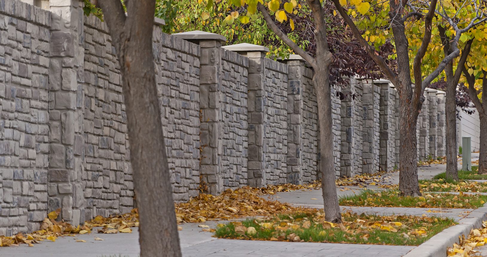 A sidewalk with trees and a stone wall.