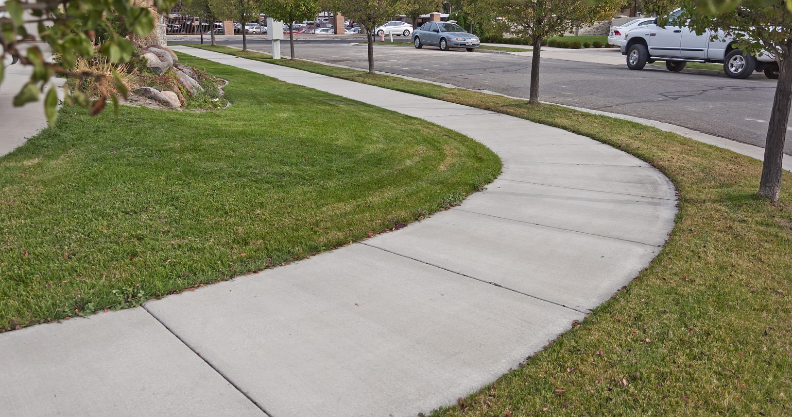 A sidewalk with grass and trees in the background.