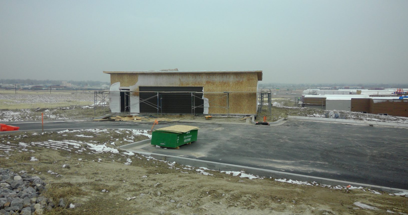 A green dumpster sitting in the middle of an empty lot.