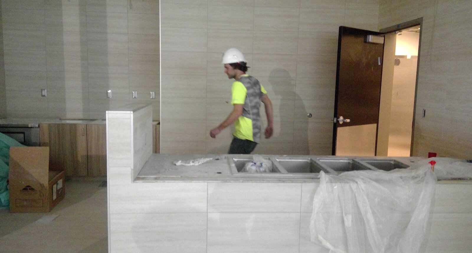 A man in yellow shirt and hard hat standing next to sink.